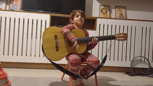 Un jeune élève assis avec une guitare classique, à la maison