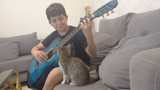 Un élève joue d'une guitare bleue sur un canapé, un chat à côté de lui