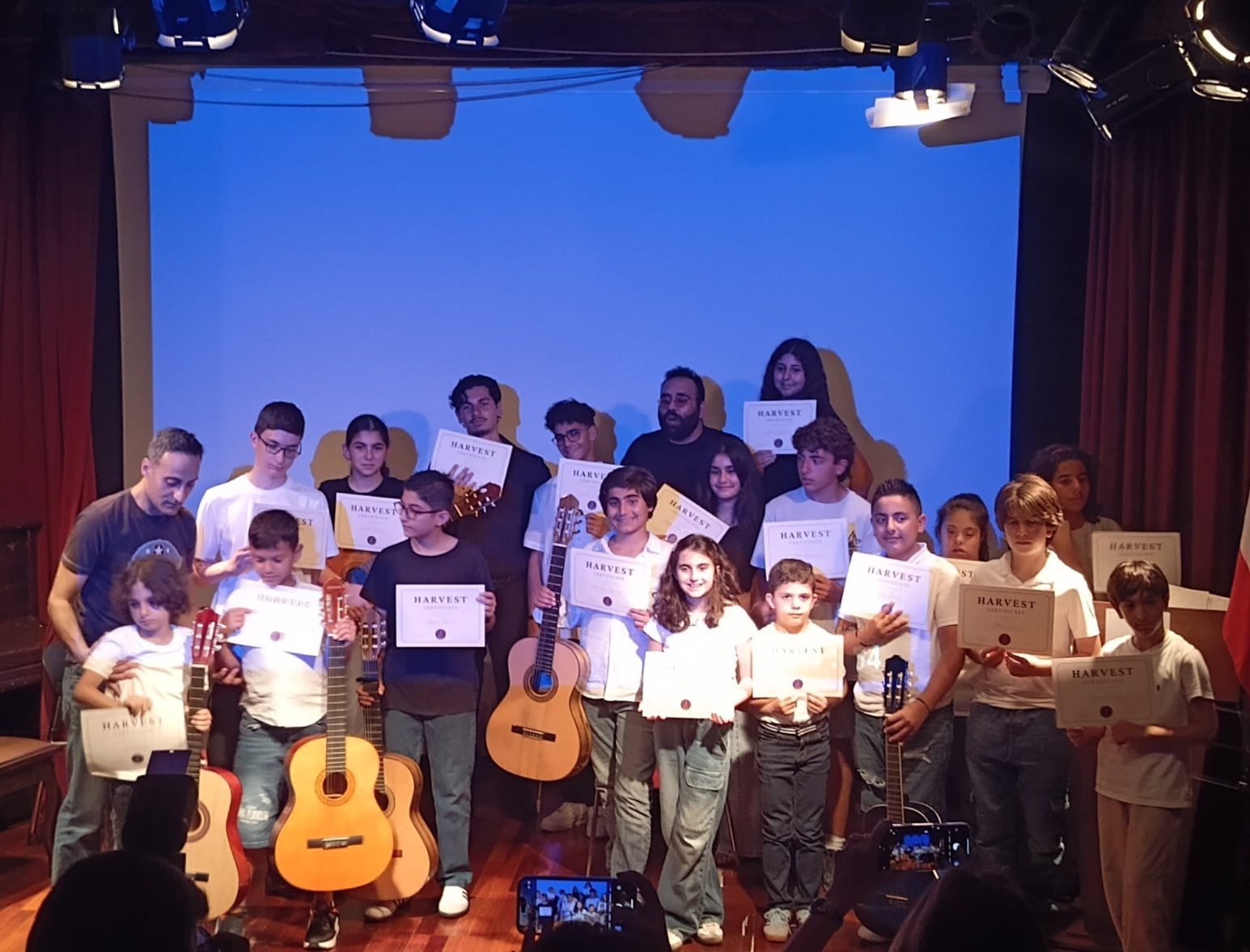 Students on stage with their guitars and certificates after the Harvest concert, June 2025