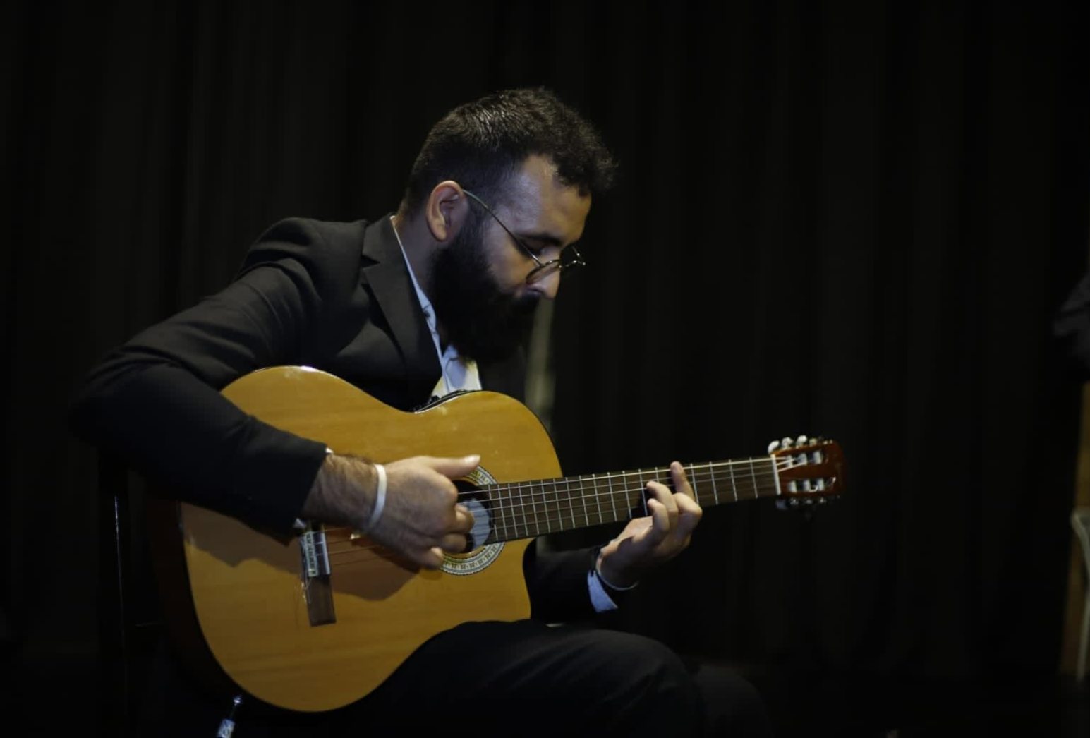 Elias Mdawwar playing classical guitar on a dark stage