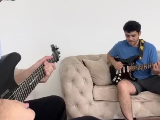 Un élève joue de la guitare électrique sur un canapé pendant un cours, son professeur à côté de lui