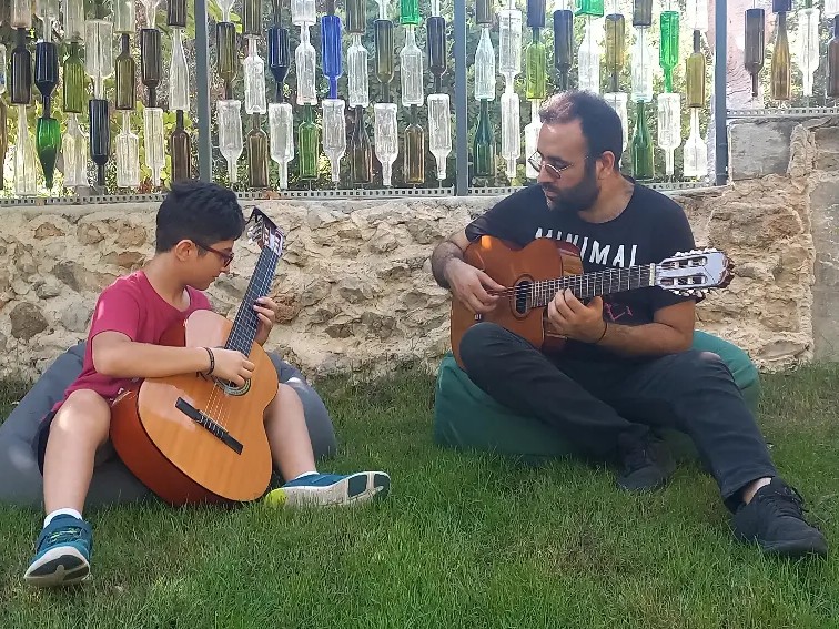 Un garçon et Elias jouent de la guitare ensemble sur l'herbe, en plein air