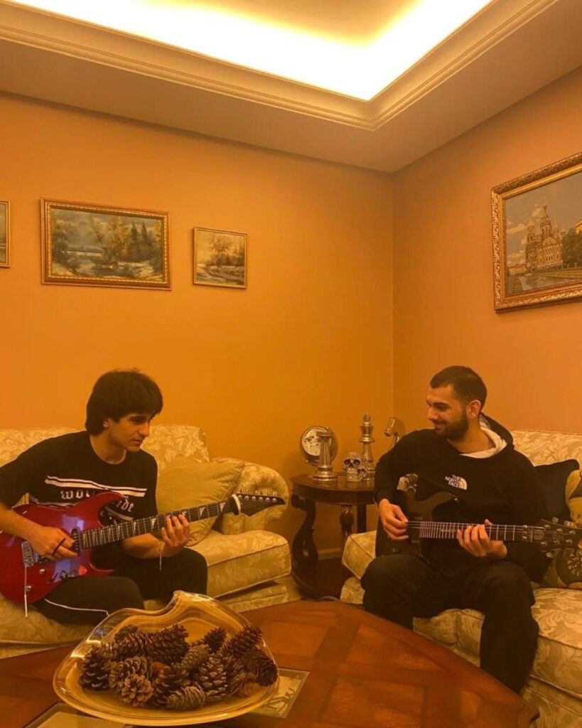 A teacher and a teenage student playing electric guitars together on a sofa at home
